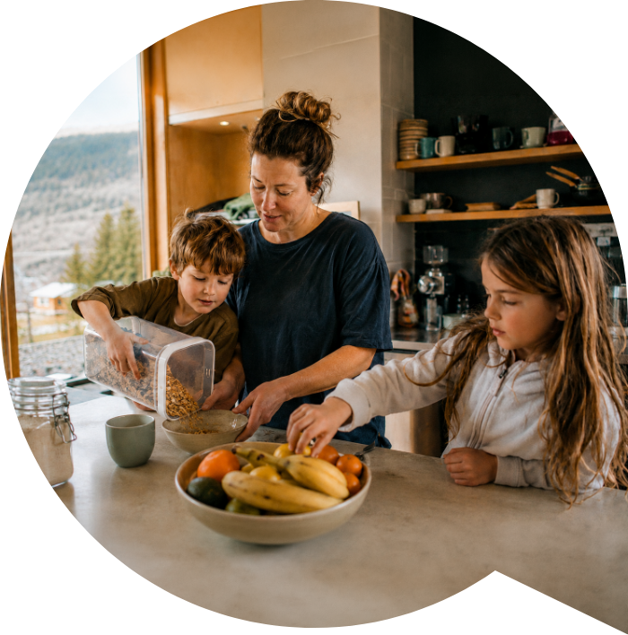A mother making breakfast with her two children in their kitchen, mountains visible through the window.